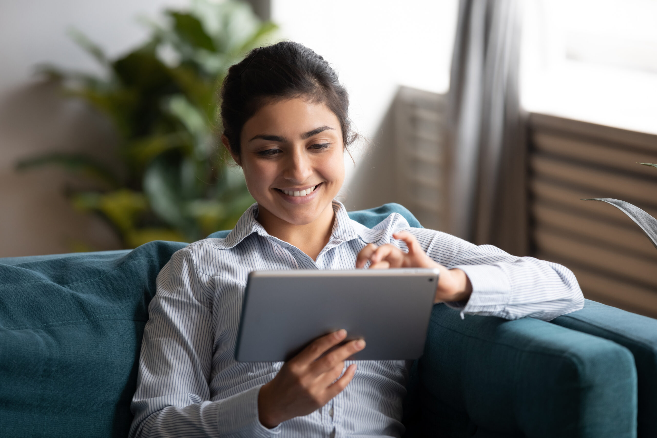 Happy indian woman using tablet sit on sofa at home Corporate AI Training